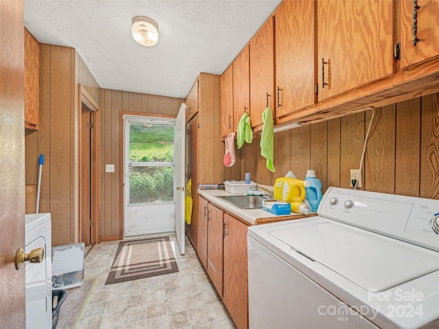 clothes washing area with wood walls, sink, washer / dryer, and cabinets