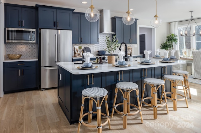 kitchen featuring hanging light fixtures, stainless steel appliances, tasteful backsplash, and wall chimney range hood