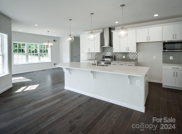 kitchen with white cabinets, wall chimney range hood, an island with sink, and appliances with stainless steel finishes