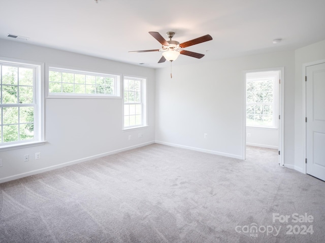 empty room featuring light colored carpet, ceiling fan, and a healthy amount of sunlight