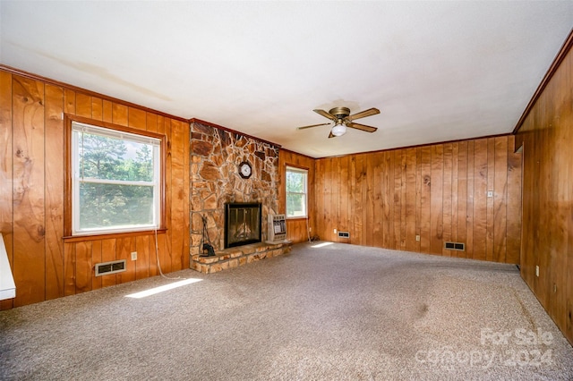 unfurnished living room with carpet flooring, ceiling fan, crown molding, a stone fireplace, and wood walls