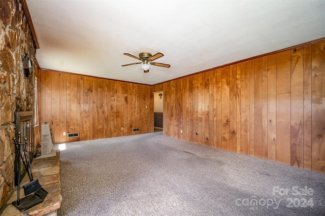 spare room featuring a fireplace, carpet floors, ceiling fan, and wood walls