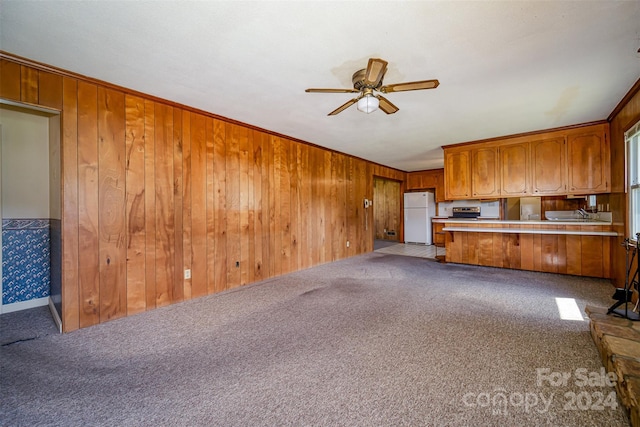 unfurnished living room with light carpet, crown molding, ceiling fan, and wooden walls