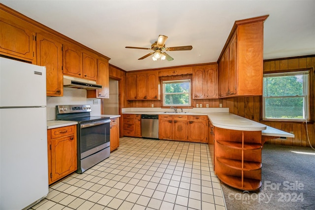 kitchen with stainless steel appliances, plenty of natural light, ceiling fan, and wooden walls