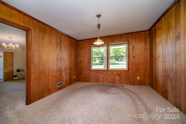 spare room featuring carpet, wood walls, crown molding, and an inviting chandelier