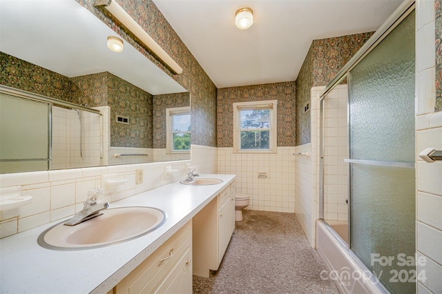 full bathroom with shower / bath combination with glass door, vanity, toilet, and tile walls