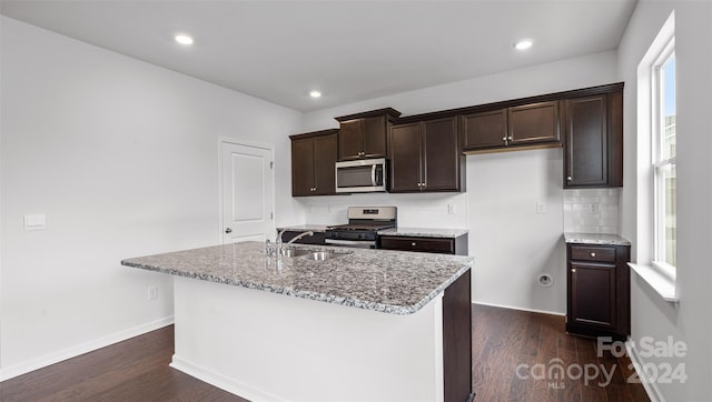 kitchen with appliances with stainless steel finishes, a center island with sink, light stone counters, and sink