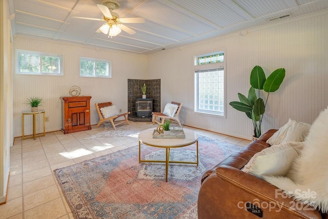 living room with a wood stove, ceiling fan, and light tile patterned flooring