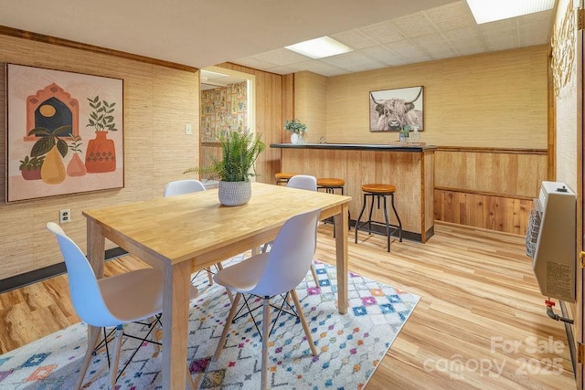 dining space featuring heating unit, wooden walls, and light hardwood / wood-style flooring