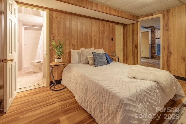 bedroom with connected bathroom, wooden walls, and hardwood / wood-style flooring