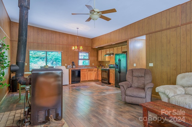 living room featuring wood walls, washer / clothes dryer, dark wood-type flooring, a wood stove, and ceiling fan with notable chandelier