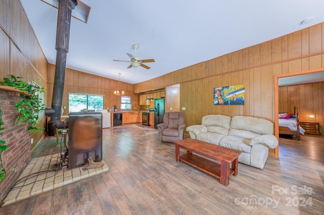 living room featuring wood walls, hardwood / wood-style floors, ceiling fan, a wood stove, and lofted ceiling