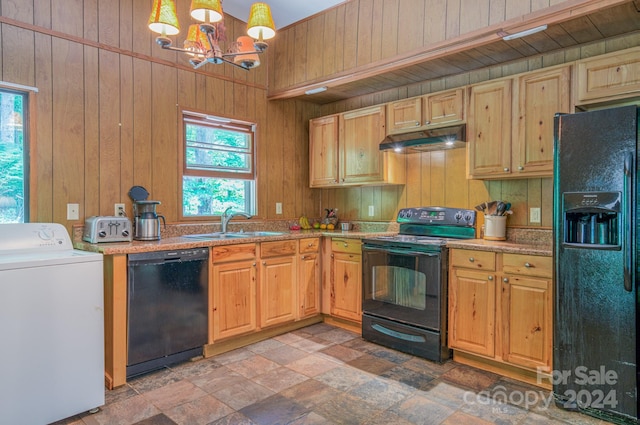 kitchen featuring wood walls, hanging light fixtures, black appliances, washer / clothes dryer, and sink