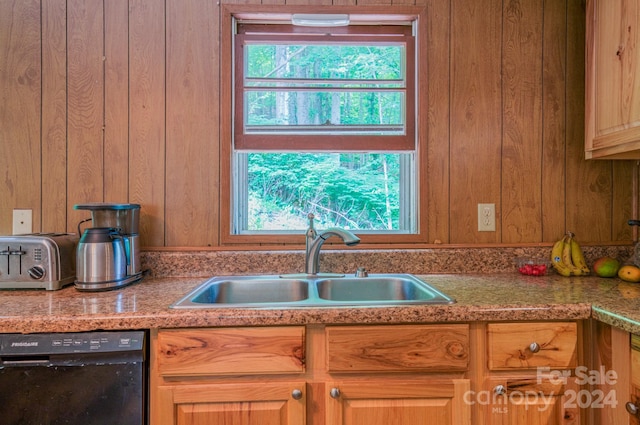 kitchen featuring sink, black dishwasher, and wooden walls