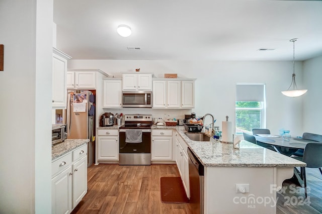 kitchen with light stone countertops, white cabinets, appliances with stainless steel finishes, decorative light fixtures, and sink