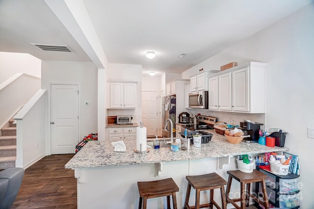 kitchen featuring appliances with stainless steel finishes, backsplash, white cabinets, and light stone countertops