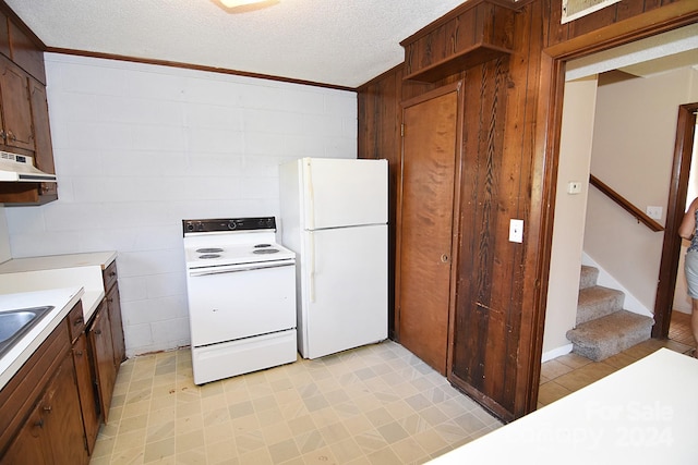 kitchen featuring a textured ceiling, wooden walls, and white appliances