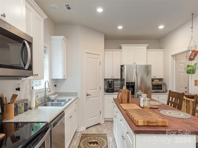 kitchen featuring white cabinets, appliances with stainless steel finishes, sink, and light wood-type flooring