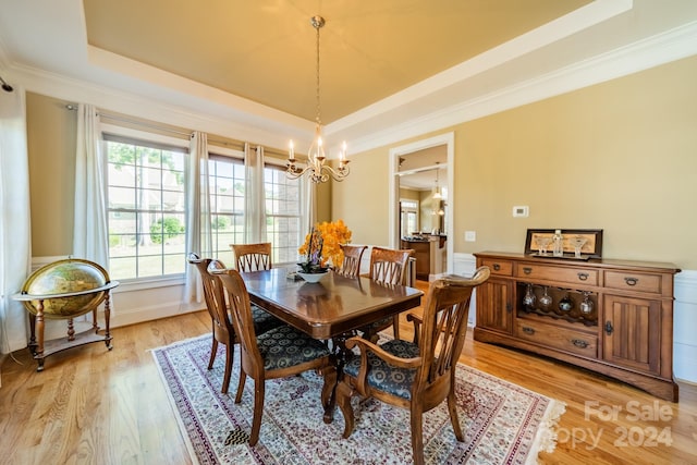 dining room featuring light hardwood / wood-style floors, a raised ceiling, crown molding, and an inviting chandelier