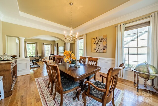 dining space with an inviting chandelier, ornate columns, a tray ceiling, plenty of natural light, and light hardwood / wood-style floors