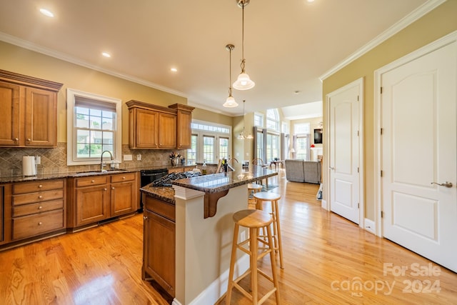 kitchen featuring sink, dark stone countertops, pendant lighting, a breakfast bar, and a kitchen island