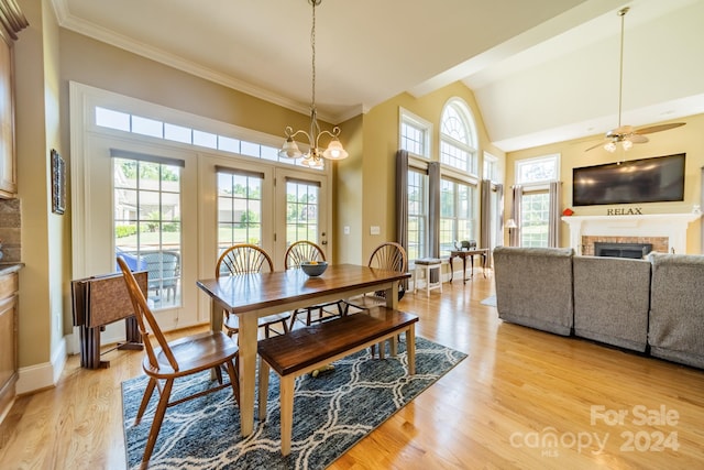 dining space with a tile fireplace, ceiling fan with notable chandelier, light hardwood / wood-style flooring, and a healthy amount of sunlight