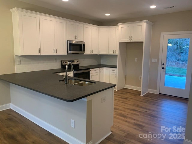 kitchen with dark wood-type flooring, sink, kitchen peninsula, appliances with stainless steel finishes, and white cabinetry