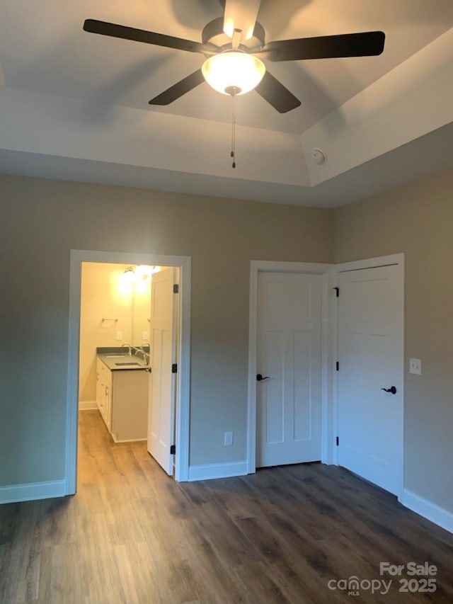 unfurnished bedroom featuring ensuite bathroom, a tray ceiling, ceiling fan, sink, and hardwood / wood-style floors