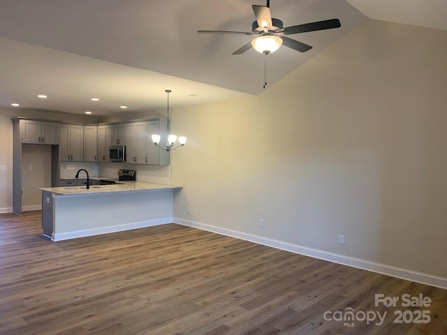 kitchen featuring kitchen peninsula, appliances with stainless steel finishes, dark hardwood / wood-style flooring, vaulted ceiling, and hanging light fixtures