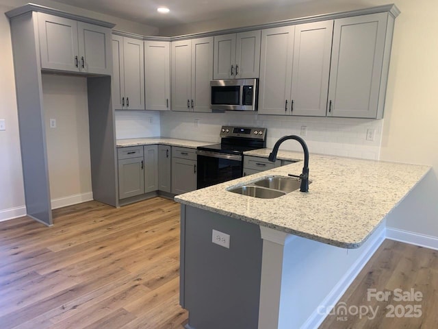 kitchen with kitchen peninsula, appliances with stainless steel finishes, light wood-type flooring, backsplash, and sink