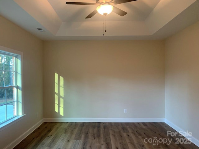 empty room with a tray ceiling, ceiling fan, and dark hardwood / wood-style flooring