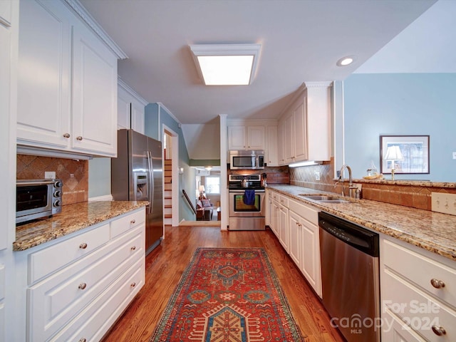 kitchen with light stone countertops, backsplash, stainless steel appliances, sink, and white cabinets