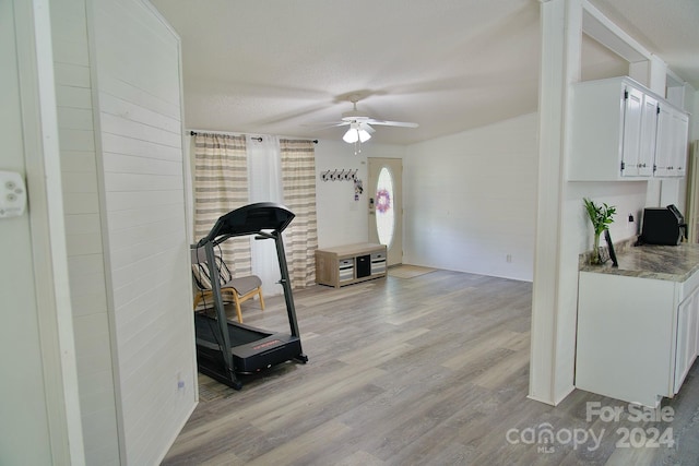 exercise area with ceiling fan, light wood-type flooring, and a textured ceiling