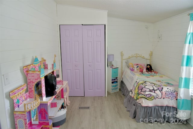 bedroom featuring lofted ceiling, a closet, wood walls, and light hardwood / wood-style flooring