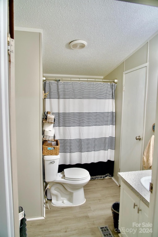 bathroom with toilet, vanity, wood-type flooring, a textured ceiling, and curtained shower