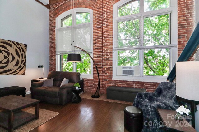 living room with a healthy amount of sunlight, dark wood-type flooring, and brick wall