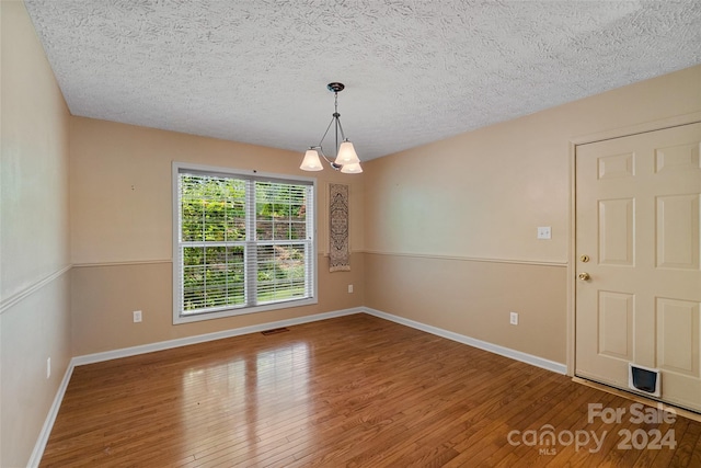 unfurnished dining area with hardwood / wood-style floors, a textured ceiling, and a notable chandelier