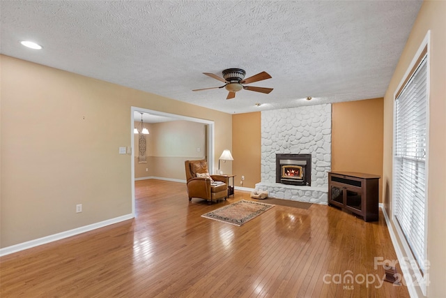 unfurnished room featuring ceiling fan, a stone fireplace, wood-type flooring, and a textured ceiling