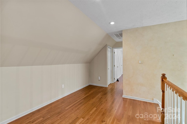 additional living space with a textured ceiling, lofted ceiling, and light wood-type flooring