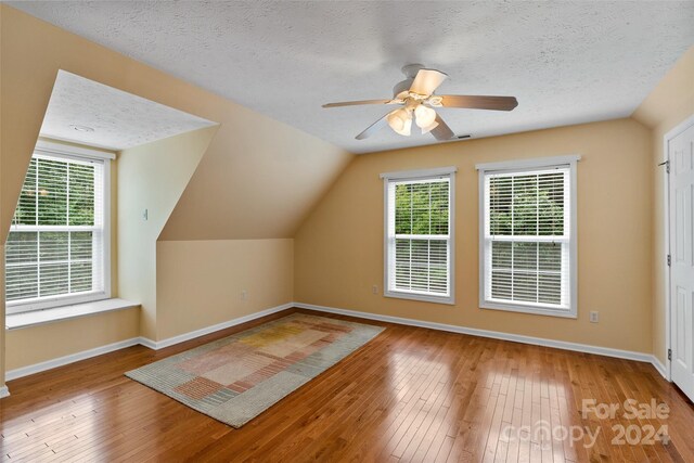 bonus room featuring vaulted ceiling, a healthy amount of sunlight, a textured ceiling, and hardwood / wood-style flooring