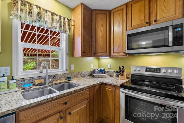 kitchen with light stone counters, sink, stainless steel appliances, and a textured ceiling