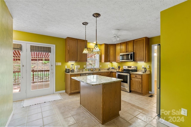 kitchen with light stone countertops, light tile patterned floors, pendant lighting, a kitchen island, and appliances with stainless steel finishes