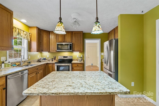 kitchen with brown cabinets, a sink, light stone counters, a kitchen island, and stainless steel appliances