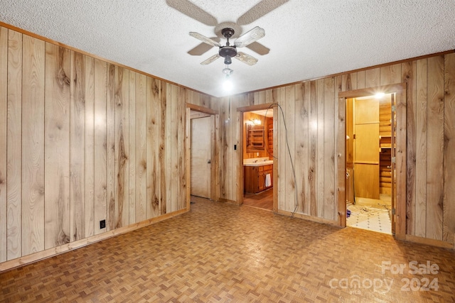 unfurnished room featuring a textured ceiling, light parquet floors, ceiling fan, and wood walls