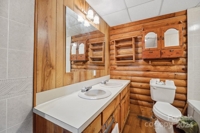 bathroom featuring a paneled ceiling, vanity, toilet, and log walls