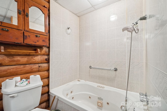 bathroom featuring log walls, tiled shower / bath, toilet, and a drop ceiling