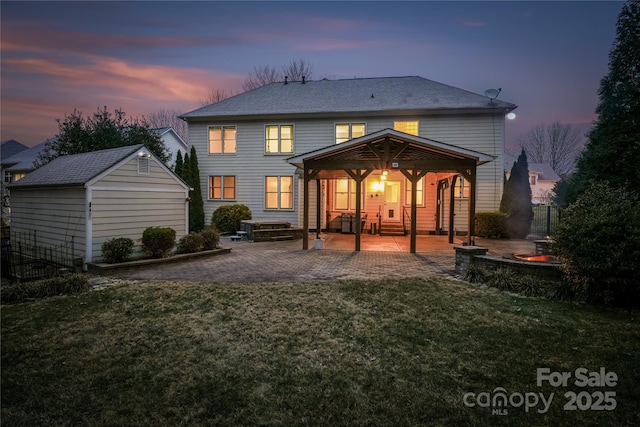 back house at dusk featuring a storage shed, a lawn, and a patio