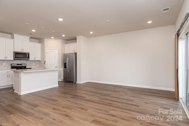 kitchen with stainless steel appliances, light hardwood / wood-style flooring, white cabinetry, and a center island with sink