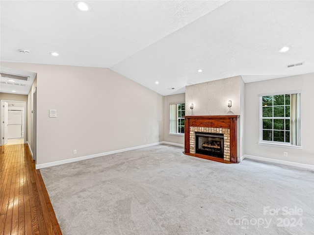 unfurnished living room featuring a fireplace, vaulted ceiling, and light colored carpet