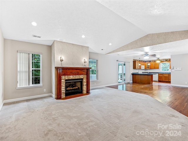 unfurnished living room with a fireplace, lofted ceiling, a textured ceiling, and a healthy amount of sunlight